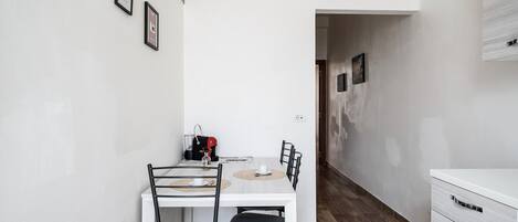 A small, modern kitchen with a white countertop, a coffee machine, and a dining table with chairs.