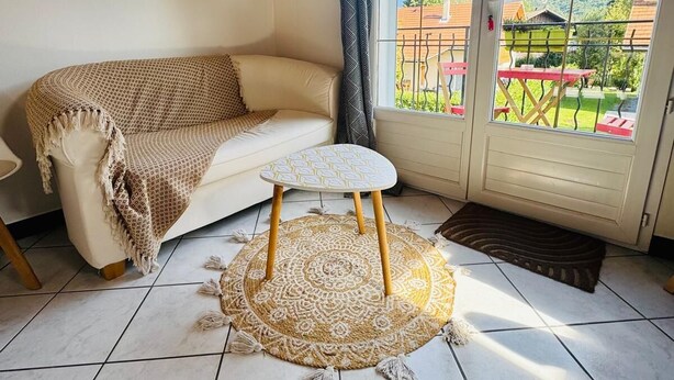 Uma sala de estar acolhedora com um sofá, uma mesa redonda pequena e vista para uma paisagem montanhosa através de uma porta de correr de vidro.
