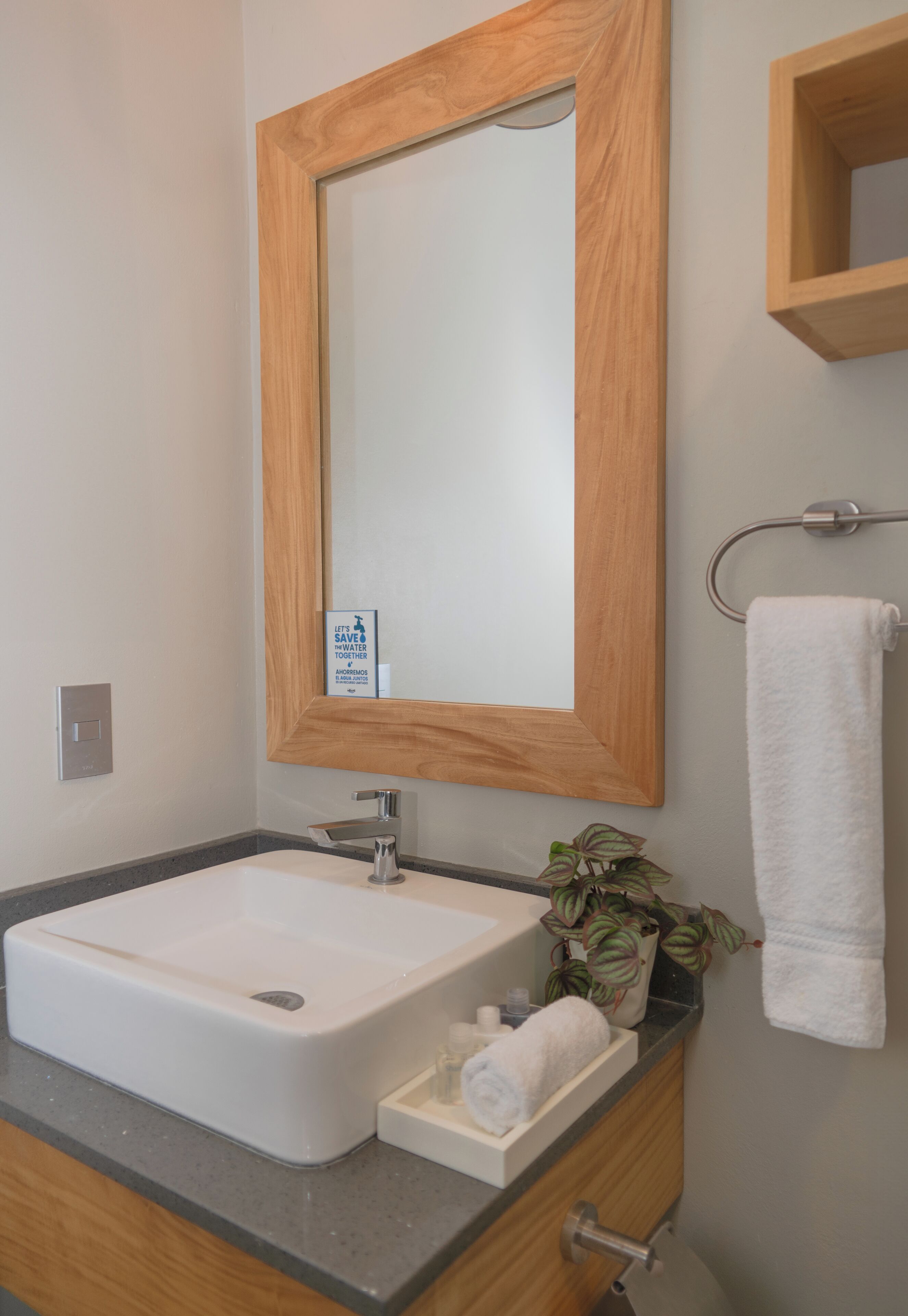 Un baño con espejo de marco de madera, lavabo blanco, toallero y planta en maceta.