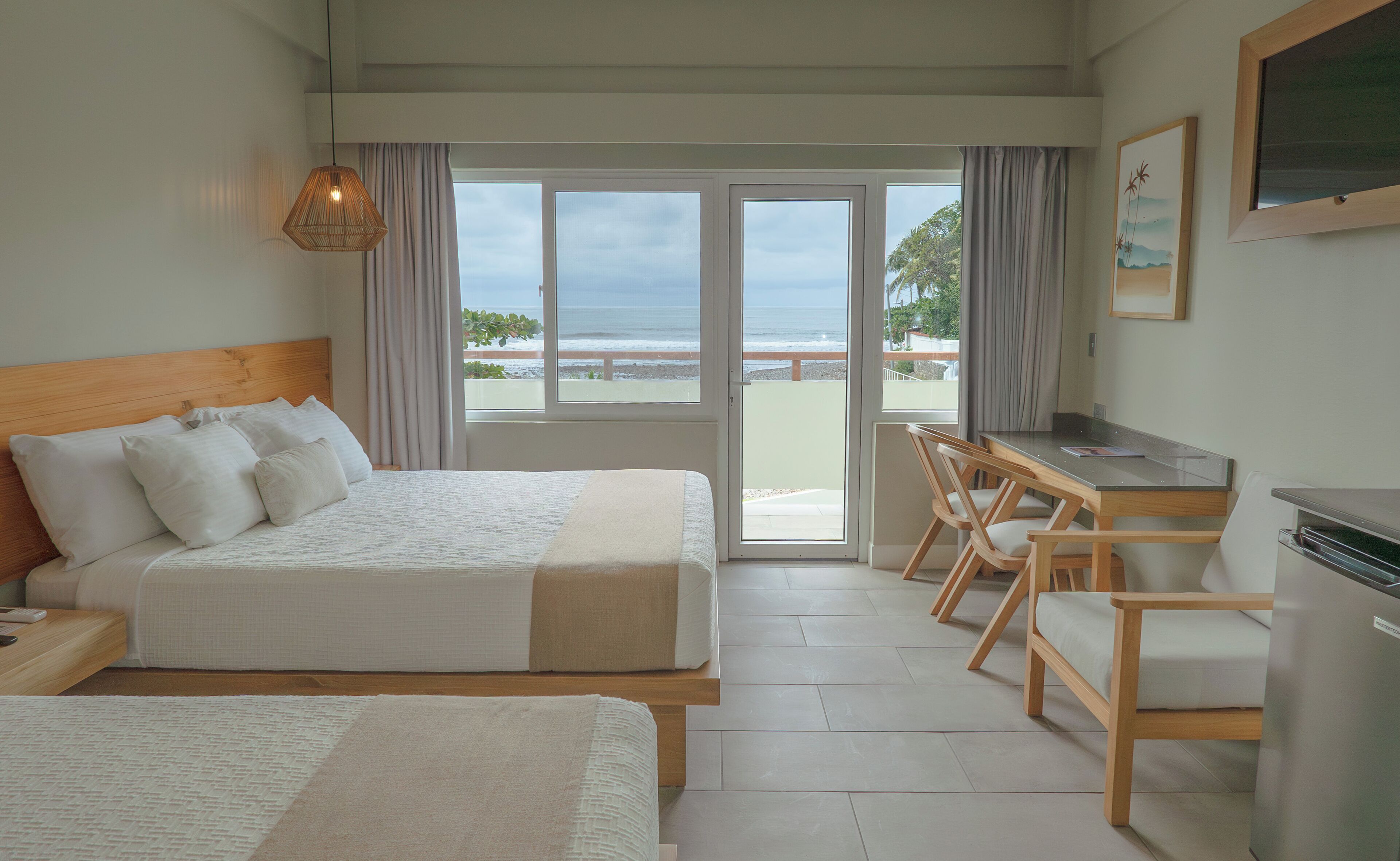 A hotel room with a bed, a desk, and a view of the beach.