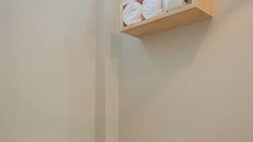 A white toilet with a white seat and lid, a toilet paper roll on the wall, and a wooden shelf with towels and a small plant.