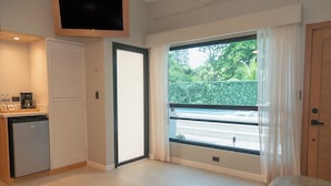 A modern hotel room with a large window, a kitchenette, and a small seating area. - Mirasurf Hotel & Waves (Tamanique)