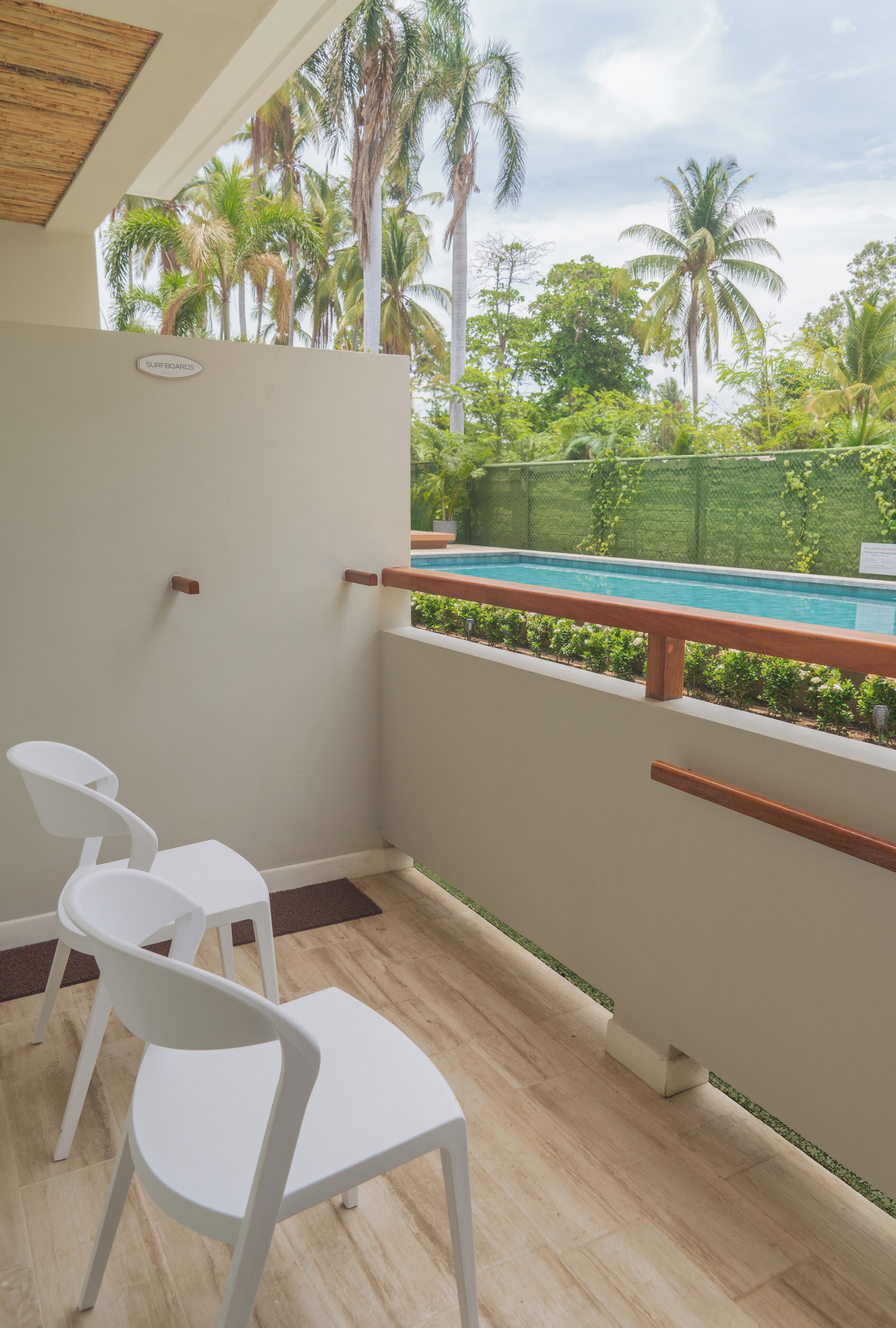 A balcony with a pool view, white chairs, and a wooden railing.