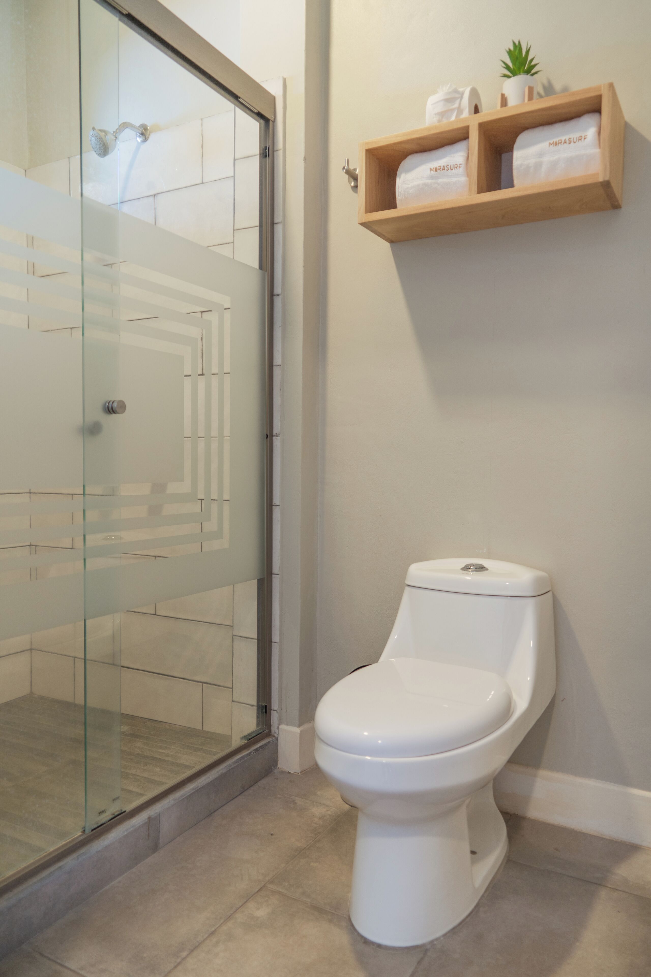 Un baño con cabina de ducha de vidrio, un inodoro blanco y un estante de madera con toallas.