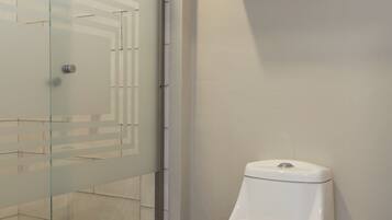Un baño con cabina de ducha de vidrio, un inodoro blanco y un estante de madera con toallas.