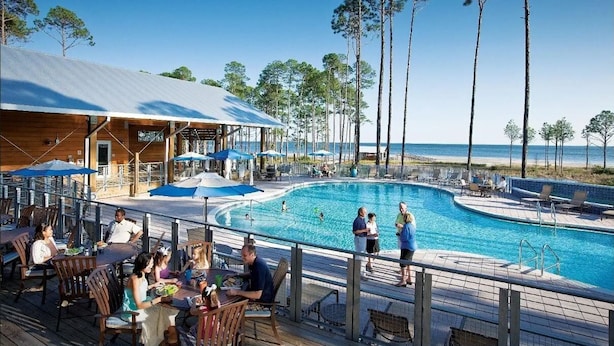 Un espace aménagé au bord de la piscine, comprenant un coin salon couvert, une piscine et une vue sur la plage.