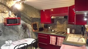 A compact kitchen with red cabinets, a microwave, a sink, and a small dining area with a table and chairs. - Le Gîte des Pêcheurs au Calme à 5 mn de Terra Botanica (Cantenay-Épinard)