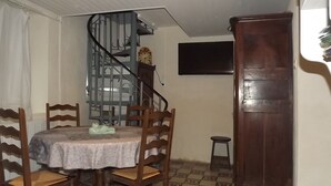 A dining area with a round table, chairs, a spiral staircase, a clock, and a wooden door. - Le Gîte des Pêcheurs au Calme à 5 mn de Terra Botanica (Cantenay-Épinard)
