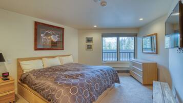A bedroom with a large bed, a dresser, a nightstand, a window with a view of trees, and a ceiling with recessed lighting.