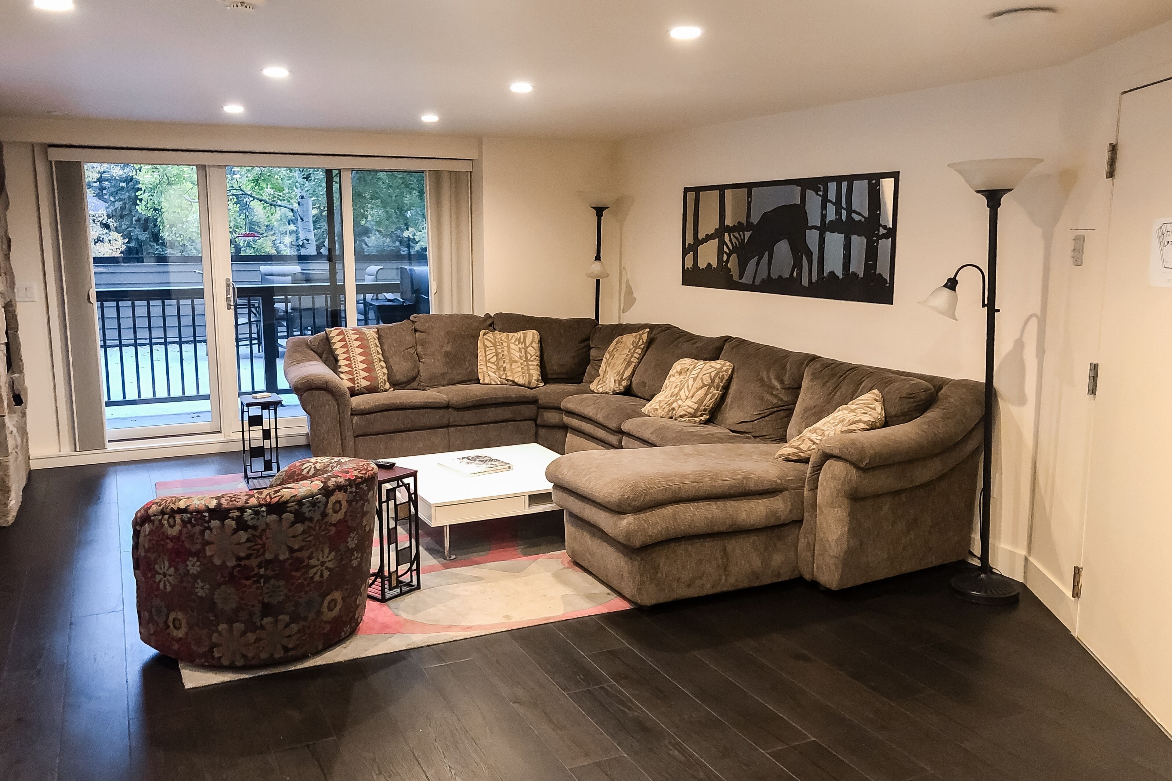 A living room with a sectional sofa, a patterned ottoman, a white coffee table, and a floor lamp.