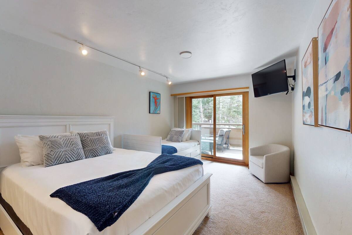 Un dormitorio con una cama grande, un televisor montado en la pared y un balcón con mobiliario exterior.