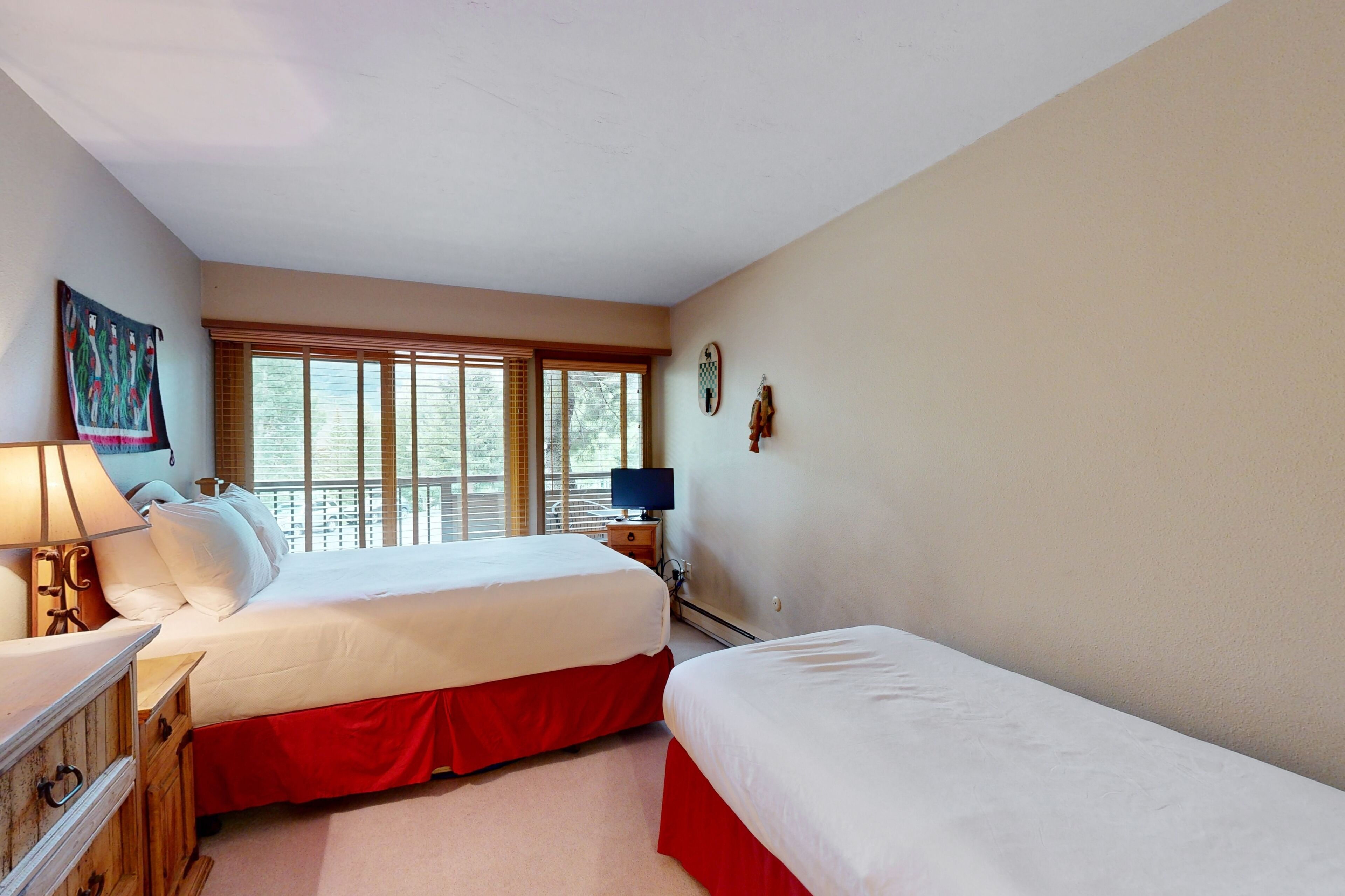A bedroom with two beds, a nightstand, a lamp, and a window with blinds.