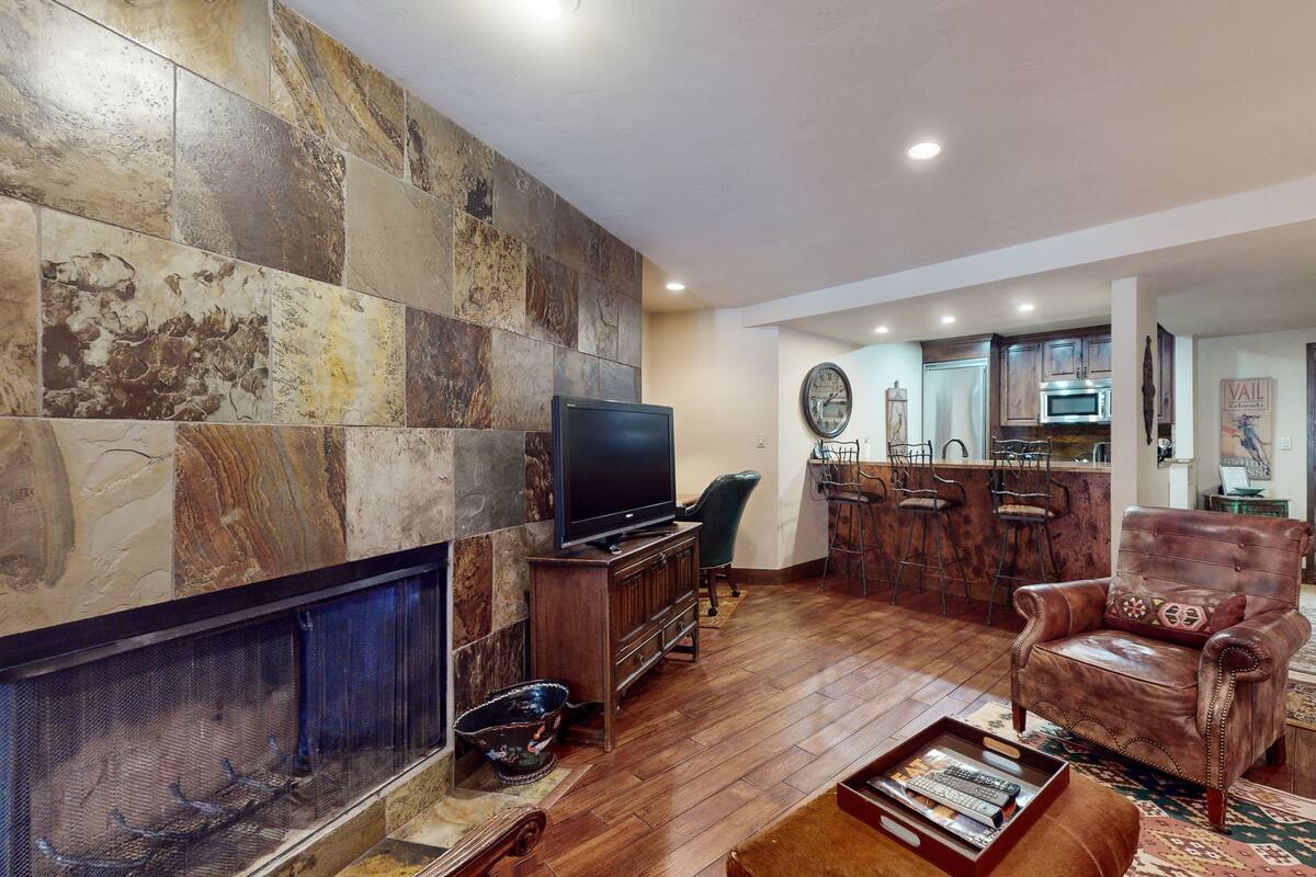 Una sala de estar con chimenea, televisor, un sillón de cuero y un comedor con barra.