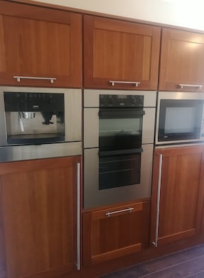 A kitchen with stainless steel appliances, wooden cabinets, and a microwave. - 2 Bedroom House Near Athy (Barrowhouse)