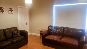 A living room with two leather sofas, wooden flooring, a white door, and a wall-mounted light fixture. - 2 Bedroom House Near Athy (Barrowhouse)