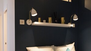 A bedroom with a bed, two bedside lamps, a shelf with decorative items, and a mirror above the bed. - 1 bedroom apartment in paris (Paris)