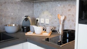 A modern kitchen with a grey hexagonal tile backsplash, a stainless steel sink, a Krups coffee maker, a wooden cutting board with cups and a pot, and a black electric stove. - 1 bedroom apartment in paris (Paris)