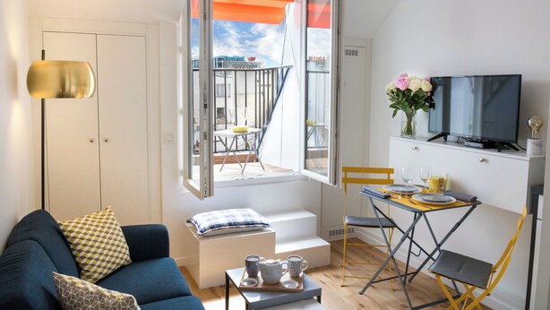 A compact living space with a sofa, a dining table, a TV, and a balcony with an orange awning. - 1 bedroom apartment in paris (Paris)