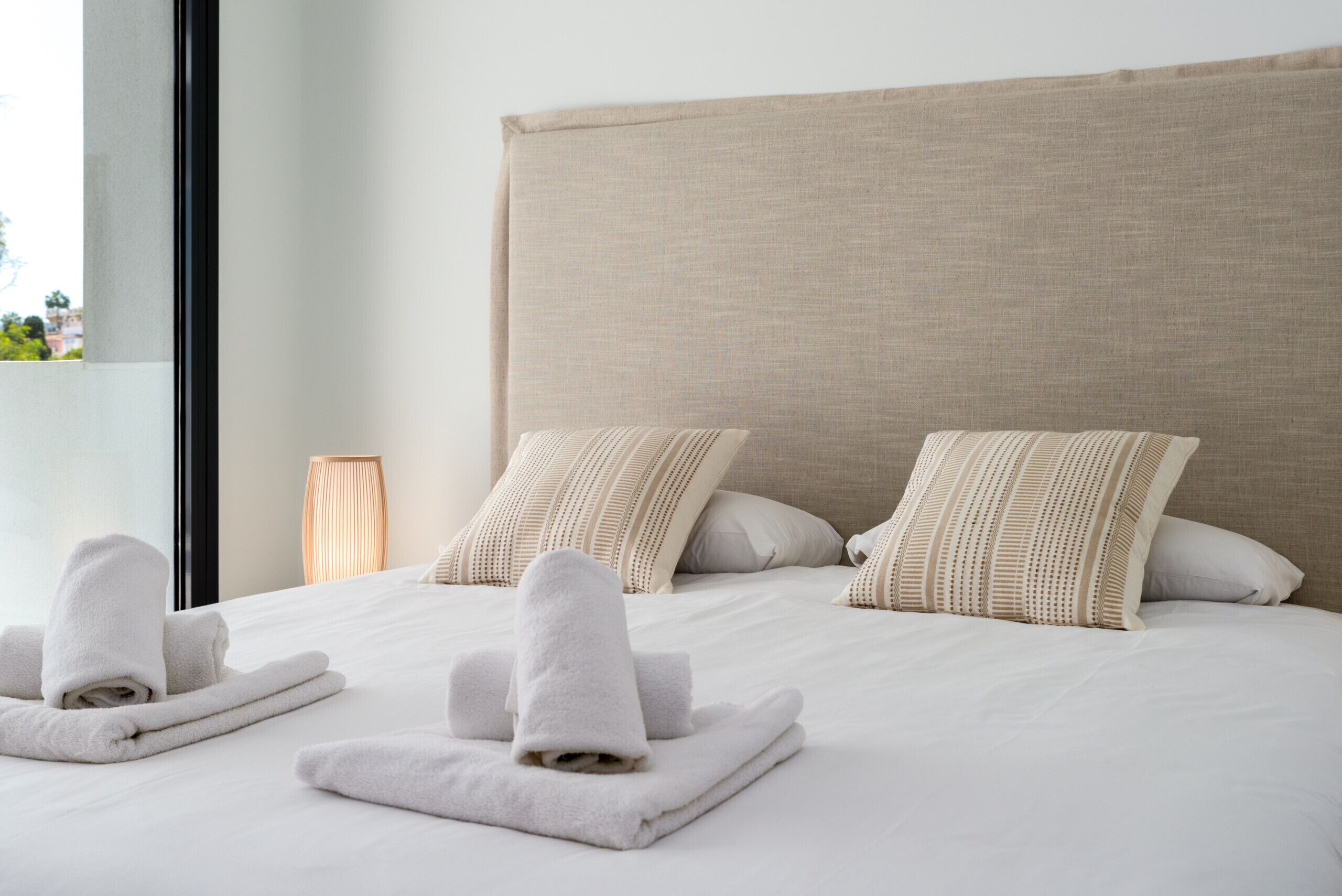 A neatly made bed with two pillows and two rolled towels.