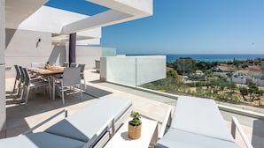 A modern outdoor dining area with a view of the sea, white furniture, and a clear sky. - Pure South II 2447 Penthouse (Manilva)