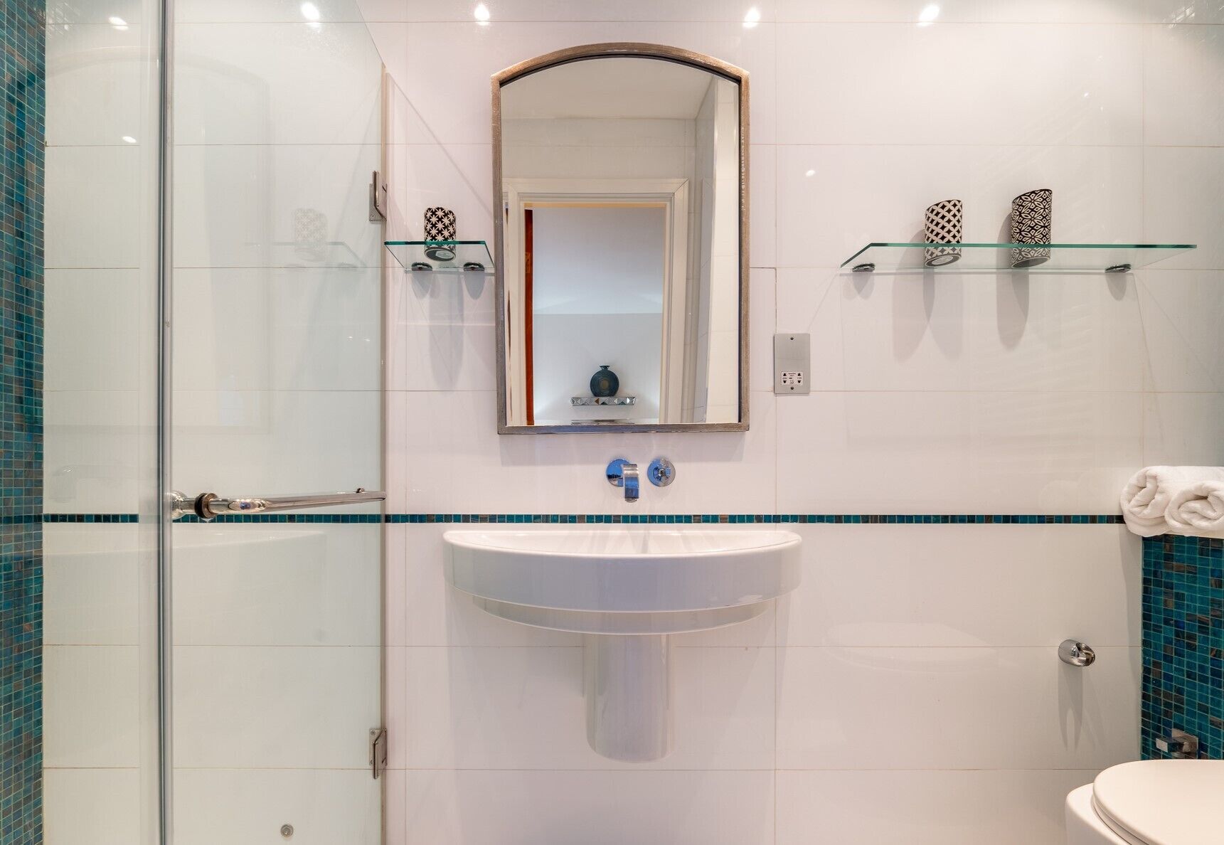 A bathroom with a glass shower enclosure, a white sink with a blue faucet, and a toilet.