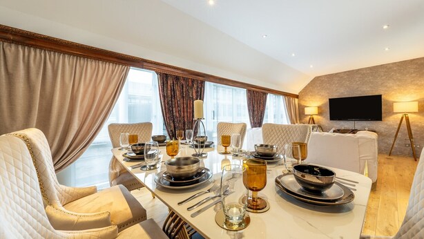 Une salle à manger avec une grande table dressée pour six personnes, agrémentée de chaises élégantes et d’un lustre moderne.