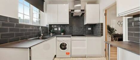 Een moderne keuken met witte kasten, een ingebouwde wasmachine en een zwart betegelde spatwand.