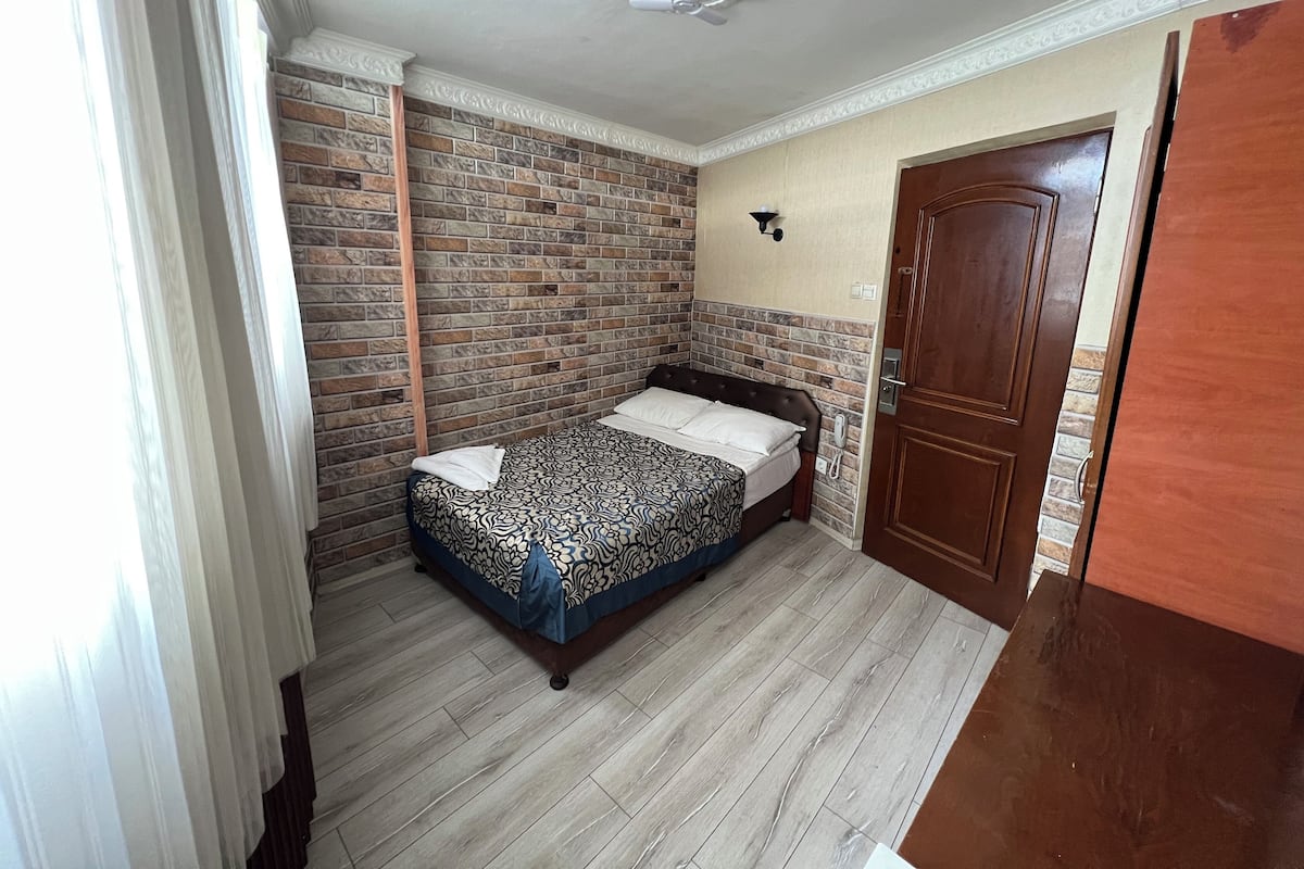 Une chambre avec un mur décoré d’un motif en briques, une porte en bois et un lit recouvert d’une literie à motifs.