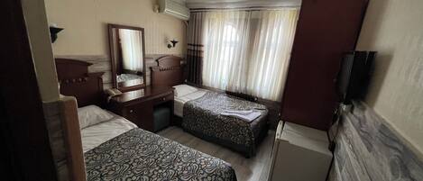 Habitación de hotel con dos camas, un escritorio con teléfono, un espejo, un televisor de pantalla plana y un ventilador de techo.
