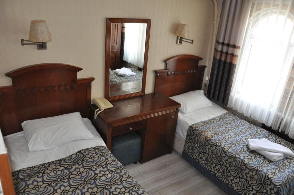 A hotel room with two beds, a desk, a mirror, and a window with curtains.
