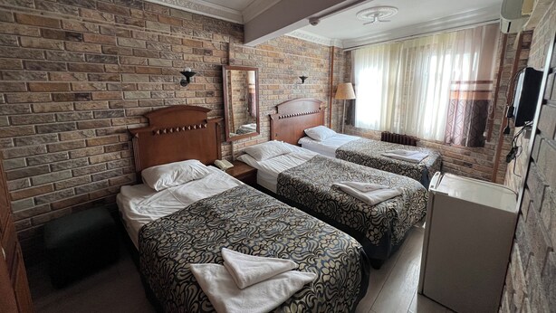 Habitación de hotel con pared de ladrillo, dos camas con ropa de cama estampada, cabecero de madera, espejo, lámpara de noche y televisor.