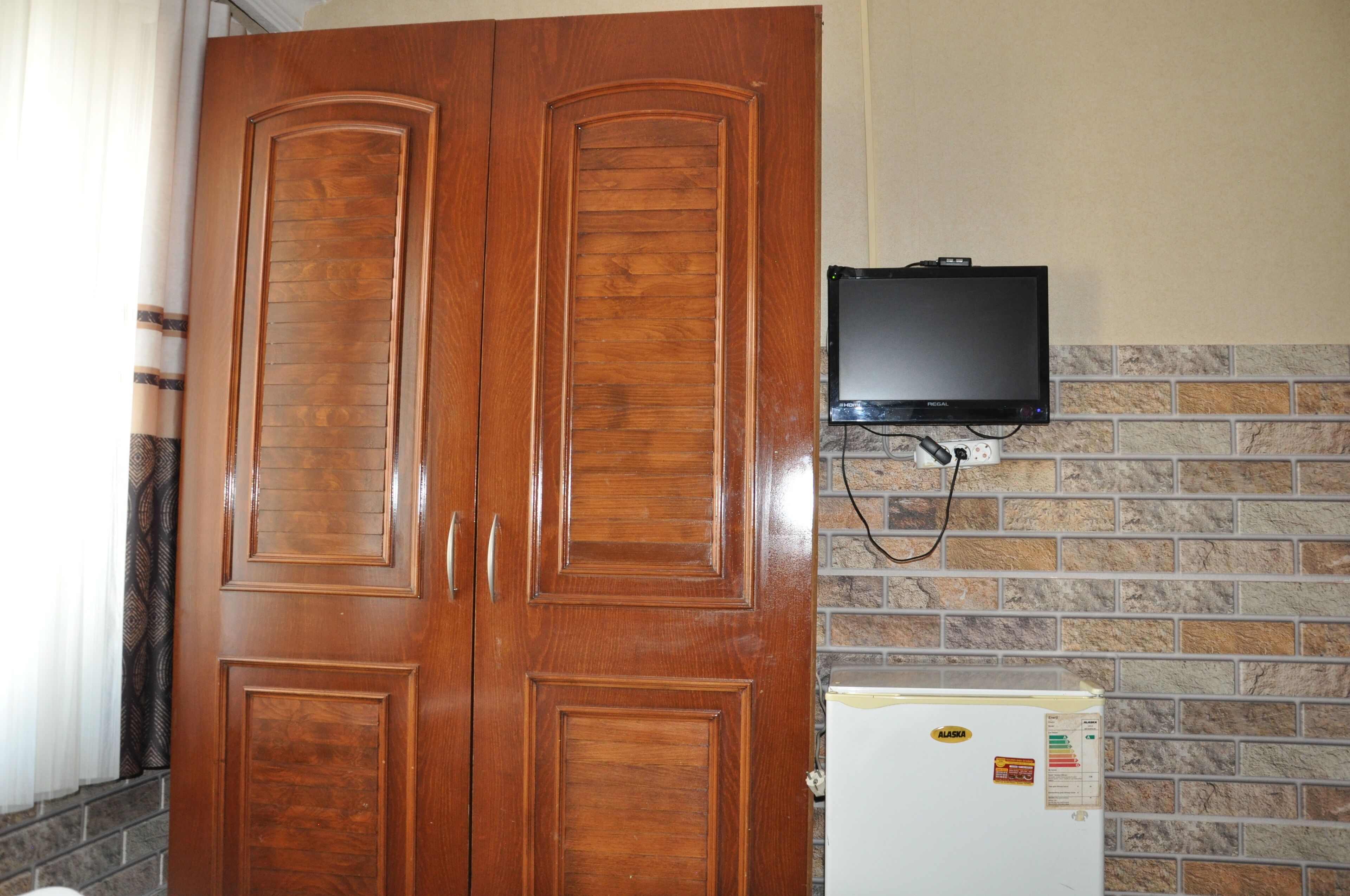 A wooden wardrobe with a television mounted on the wall above it.