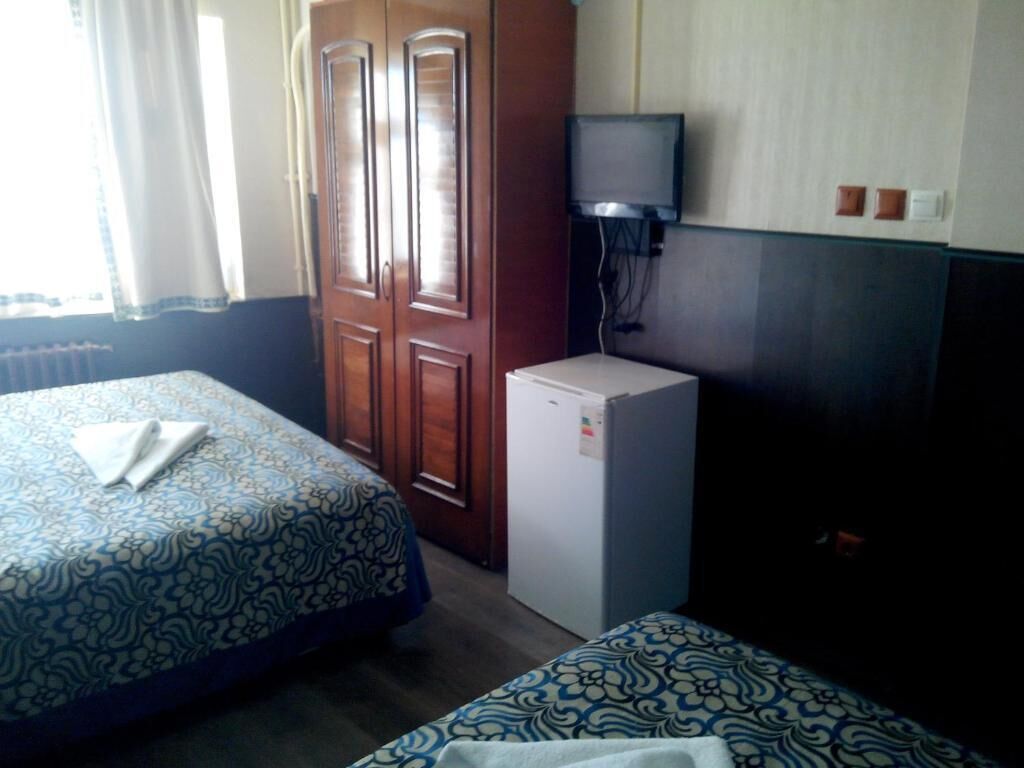 A hotel room with two beds, a small refrigerator, a television, and a wooden wardrobe.