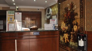 Zona de recepción de un hotel con un mostrador de madera, un reloj y un cuadro grande con motivos florales en la pared.