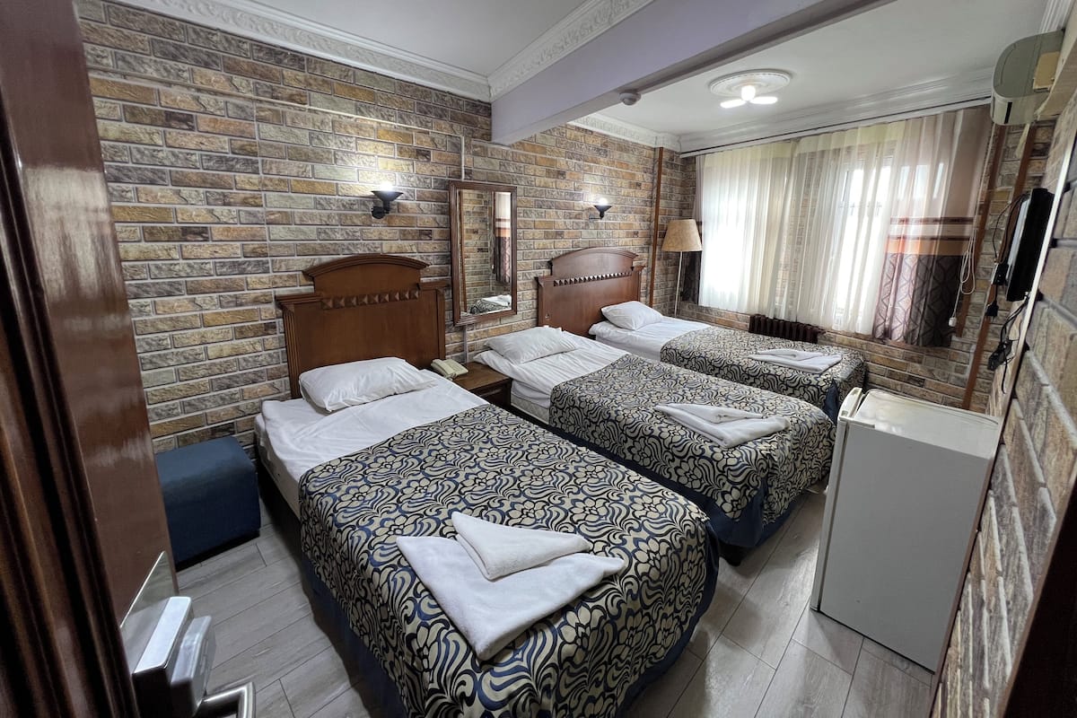Une chambre d’hôtel avec trois lits, un mur décoré d’un motif en pierre, un miroir et un ventilateur de plafond.