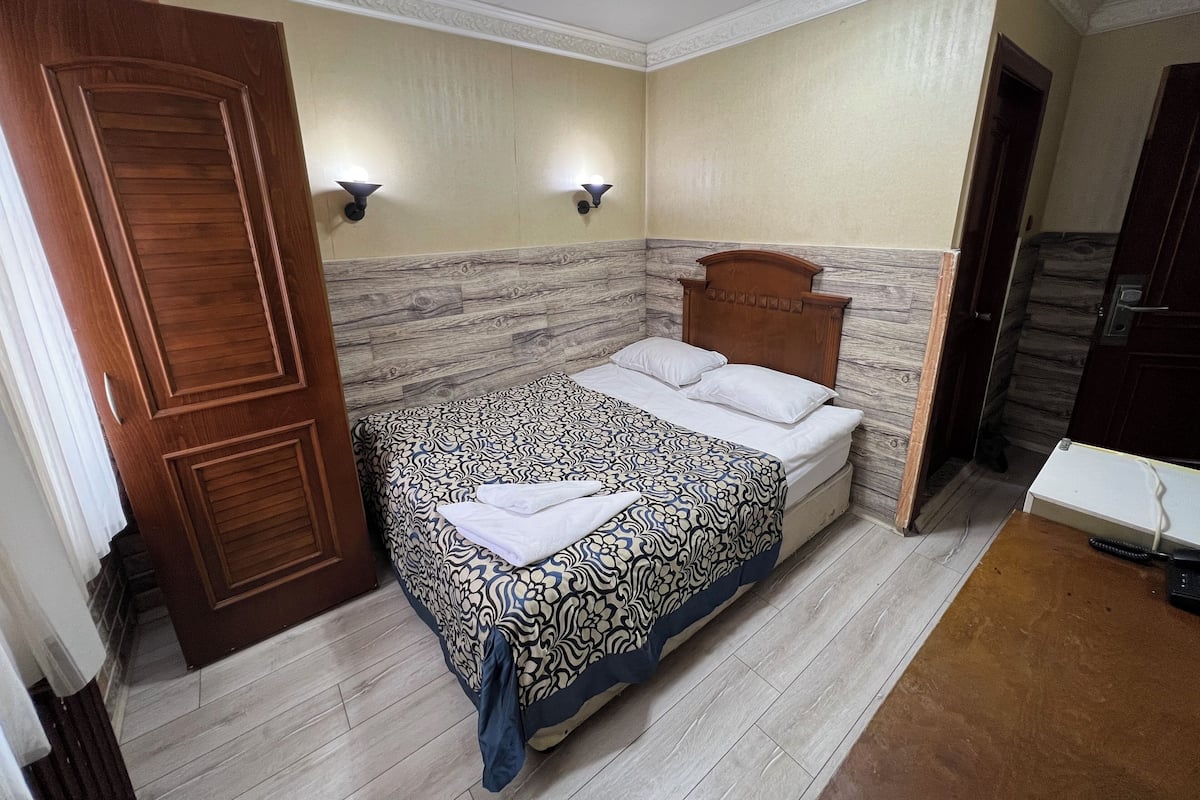 Une chambre à coucher avec un lit, une tête de lit en bois, deux lampes fixées au mur et une porte.