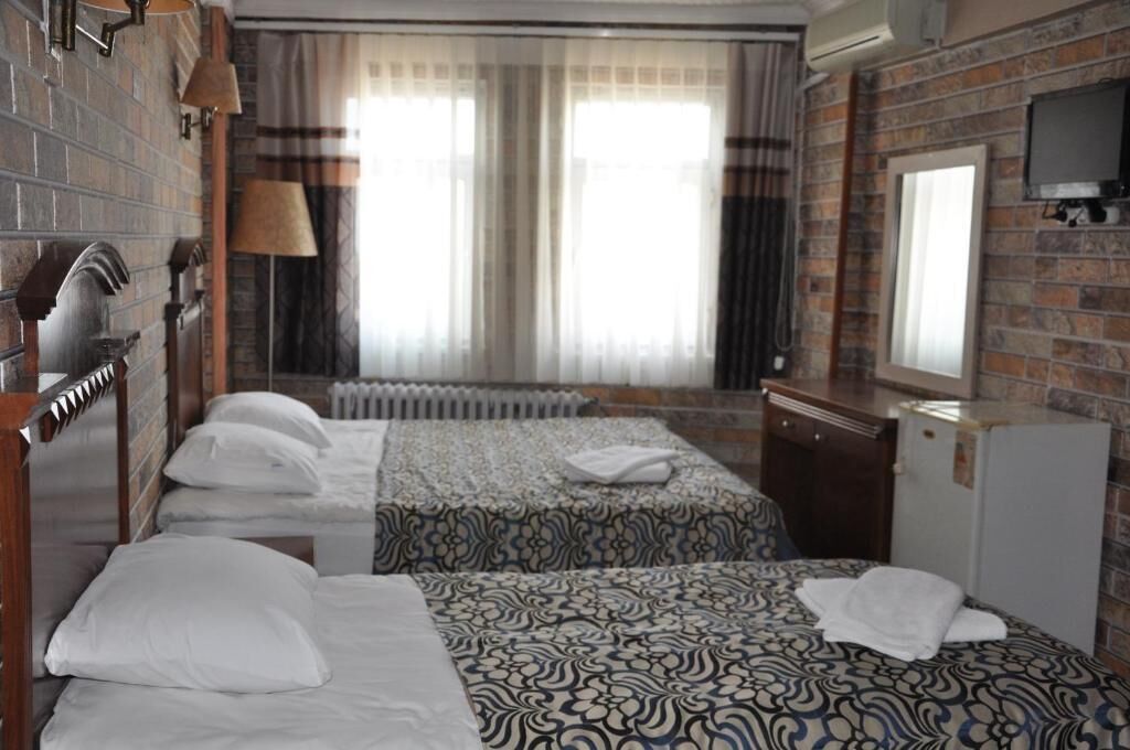 A hotel room with two beds, a wooden headboard, a radiator, a television, and a window with curtains.