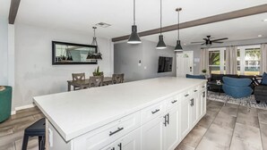 Une cuisine moderne dotée d’un grand îlot central, de luminaires suspendus et d’un coin repas avec une table et des chaises.