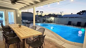 Un espace extérieur avec une piscine, une table et des chaises en bois, un ventilateur de plafond et une vue sur la piscine.
