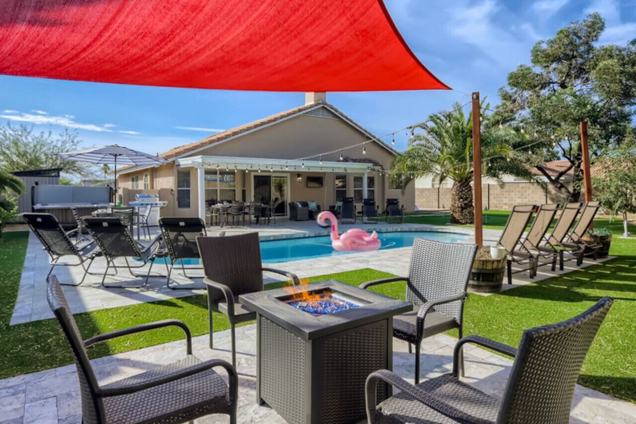 Un patio trasero con piscina, sillas de descanso, una chimenea y un porche cubierto.