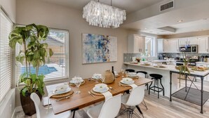 A modern kitchen with white cabinets, a central island, and a dining area with a wooden table set for six. - Pickle Ball, Heated Pool, Spa, Outdoor Bar w/Swings, Game Room, Bocce, & Putt-Putt! (Scottsdale)