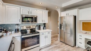 A modern kitchen with white cabinetry, stainless steel appliances, and a wooden floor. - Pickle Ball, Heated Pool, Spa, Outdoor Bar w/Swings, Game Room, Bocce, & Putt-Putt! (Scottsdale)