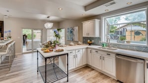 A modern kitchen with white cabinets, a large window, and a dining area with a table set for a meal. - Pickle Ball, Heated Pool, Spa, Outdoor Bar w/Swings, Game Room, Bocce, & Putt-Putt! (Scottsdale)