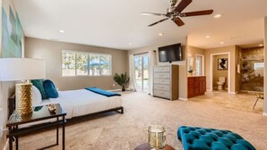 Une chambre spacieuse comprenant un lit, un bureau, une chaise, un ventilateur de plafond et un téléviseur.