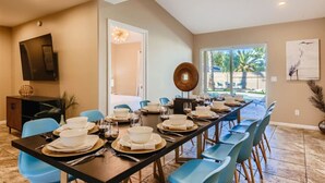Un coin repas avec une longue table dressée pour le repas, des chaises bleues et une vue sur l’extérieur.