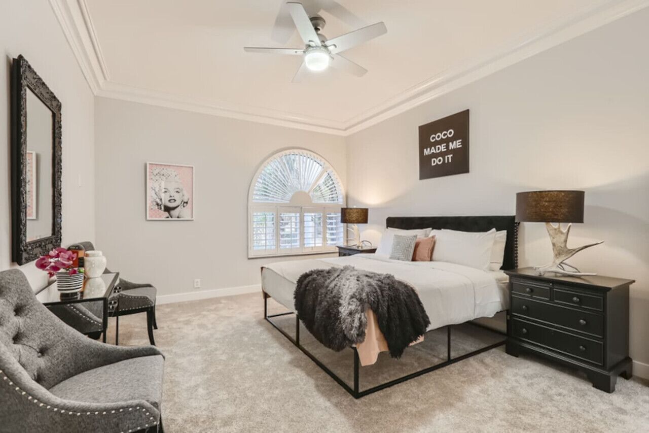 Ein Schlafzimmer mit einem Bett, Nachttischen, einem Sessel, einem Deckenventilator und einem Fenster mit Jalousien.