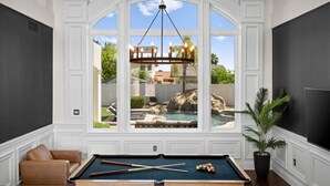 Sala com mesa de bilhar, uma poltrona confortável e uma grande janela com vista para a piscina e o jardim.