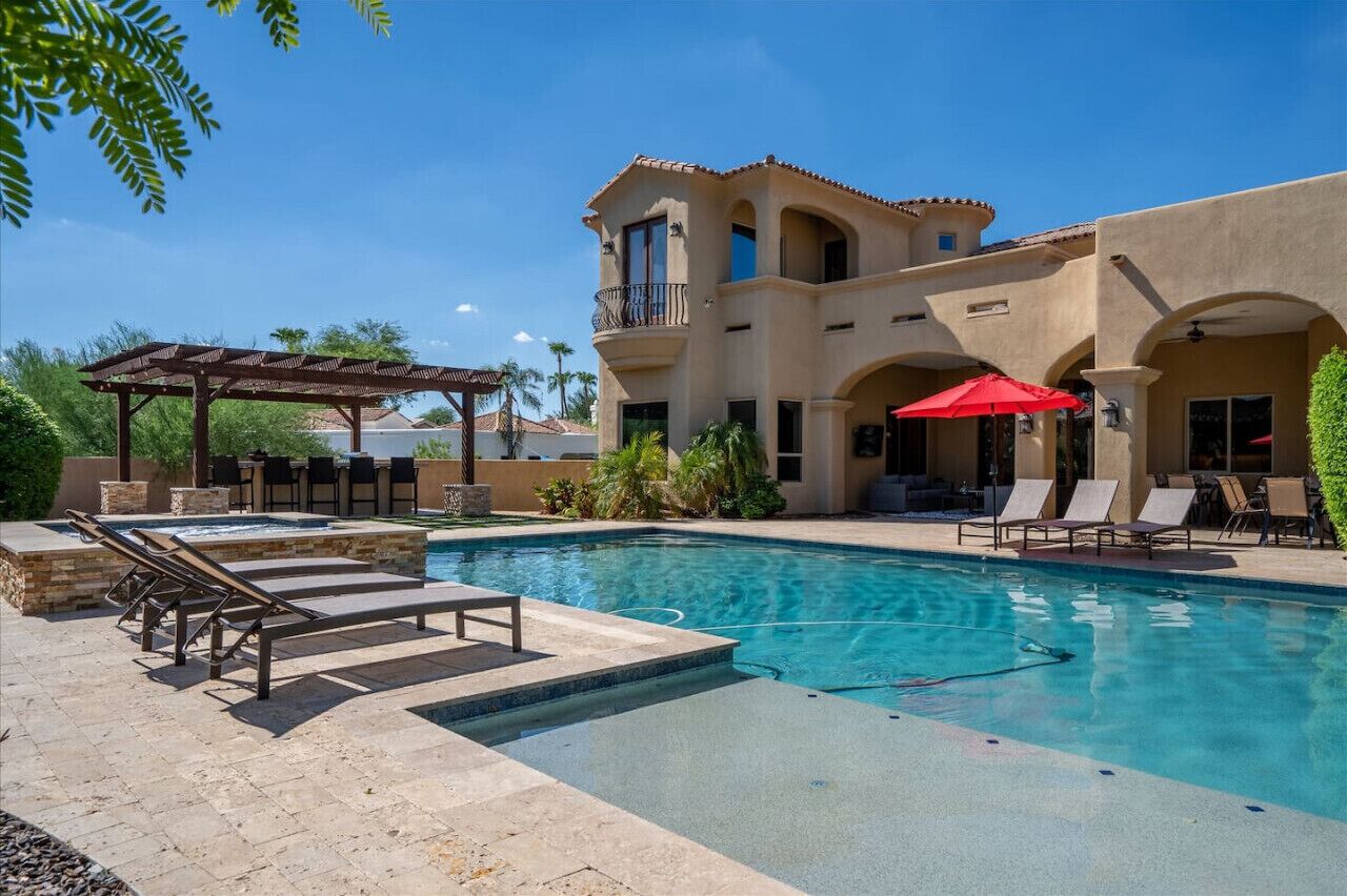 A pool area with lounge chairs, a hot tub, and a covered seating area.