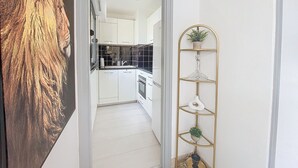 A hallway leading to a kitchen with white cabinets, a black backsplash, and a gold decorative shelf with plants. - N&J - POP ART - Central - Balcony (Niza)