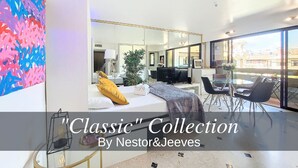 A modern hotel room with a large bed, a sitting area with a coffee table, a dining area with chairs, and a large window offering a view. - N&J - POP ART - Central - Balcony (Niza)